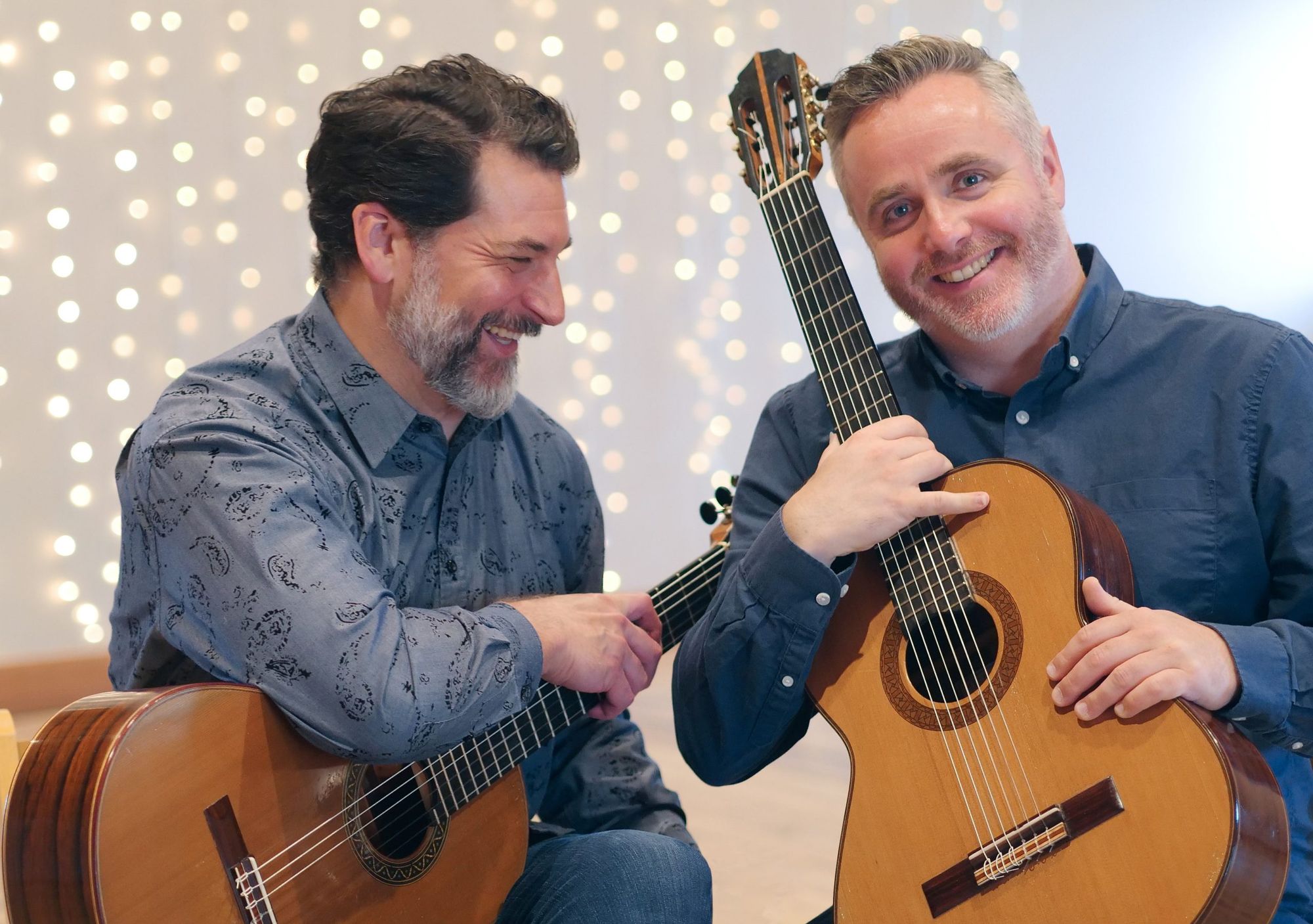 Matthew Cochran and Matthew McAllister laughing with their guitars in front of a wall of lights